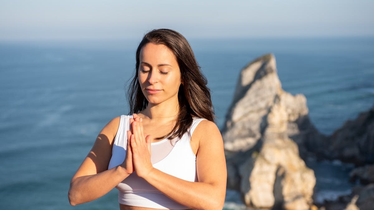 Woman meditating outdoors by the ocean in Portugal, promoting relaxation and mindfulness.